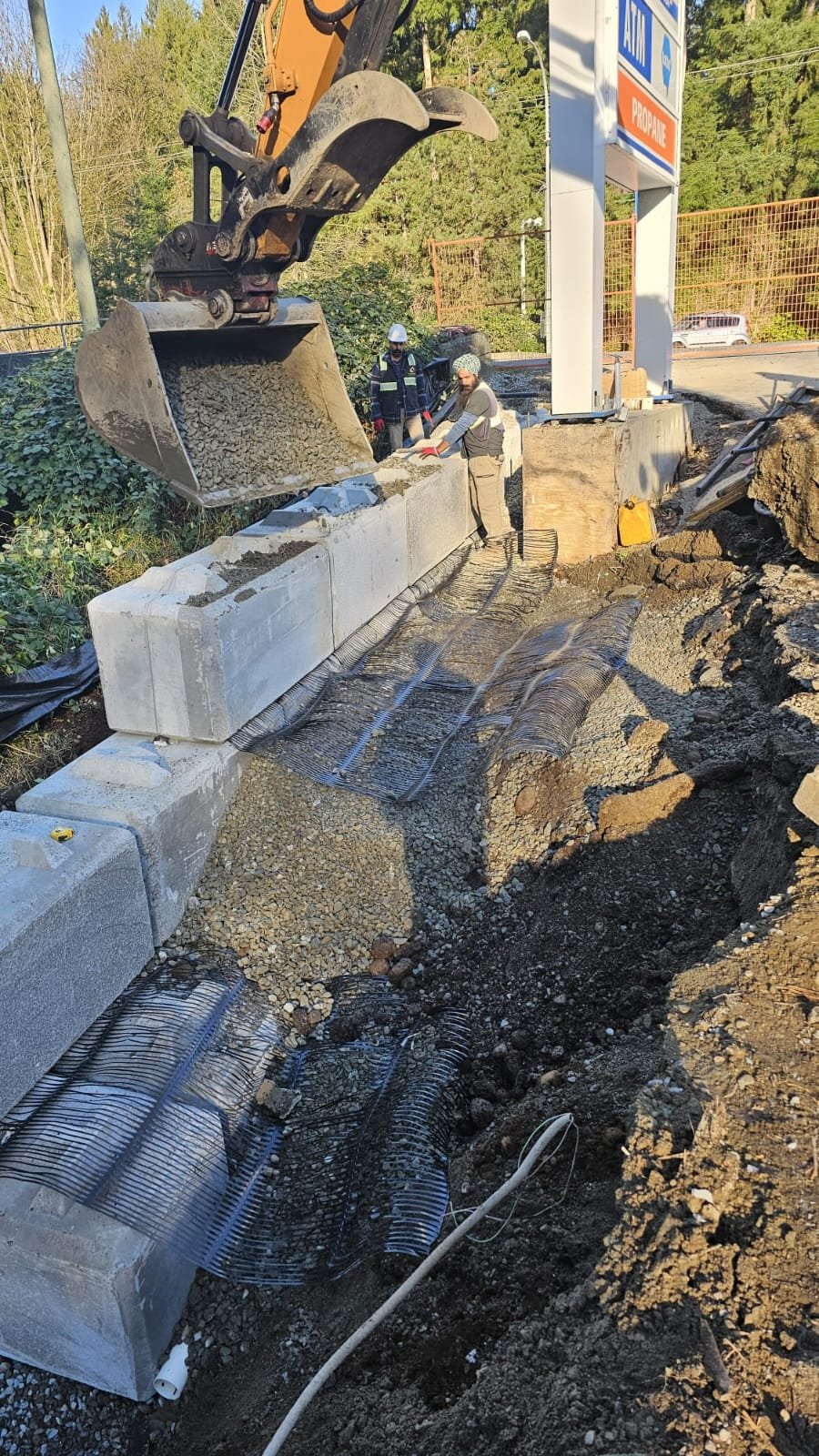 Excavator pouring gravel behind lock-block retaining wall